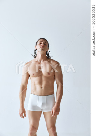 Portrait of handsome man with braids, muscular strong body standing shirtless in underwear against grey studio background 105526533