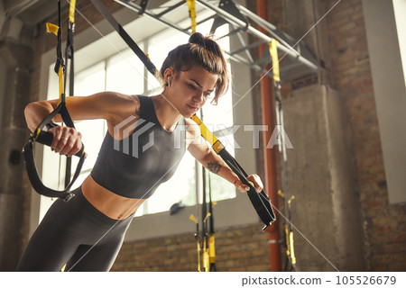 Perfect push-up. Side view of young athletic woman with perfect body in sportswear doing push ups with trx fitness straps in the gym. Perfect push-up. Side view of young athletic woman with perfect body in sportswear doing push ups with trx fitness straps in the gym. 105526679