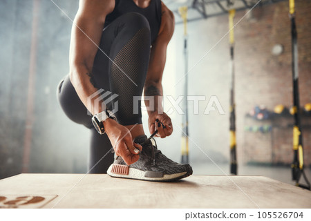 Preparing for workout. Cropped photo of beautiful young woman in sports clothing tying her shoelaces while exercising in gym. Preparing for workout. Cropped photo of beautiful young woman in sports clothing tying her shoelaces while exercising in gym. 105526704