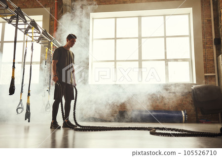 Never stop. Side view of young athletic man with perfect body doing crossfit exercises with a rope in the gym. 105526710