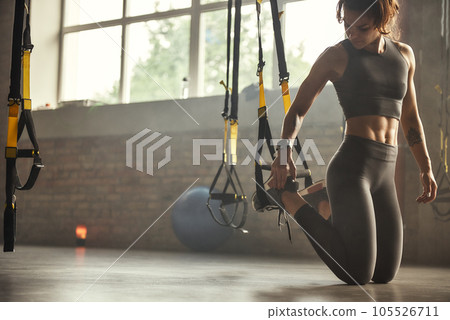 Young athletic woman in sports clothing adjusting trx fitness straps while training in the gym. Young athletic woman in sports clothing adjusting trx fitness straps while training in the gym. 105526711