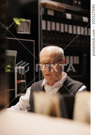 Senior private detective working at criminal case late at night in arhive room, analyzing mysterious victim report. Elderly police officer checking crime scene evidence, confidential information 105527040