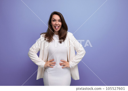 cheerful brunette woman in ivory jacket and white dress posing in studio 105527601