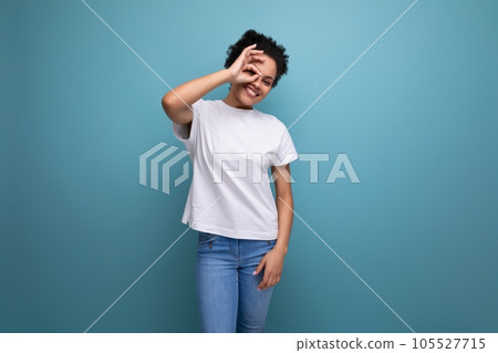 surprised young brunette woman with afro hair in a white t-shirt uses her hands for gesticulation surprised young brunette woman with afro hair in a white t-shirt uses her hands for gesticulation 105527715
