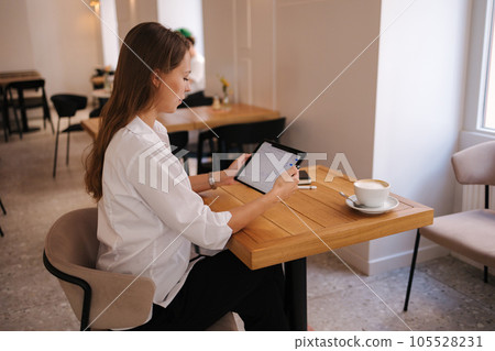 Side view of female freelancer working in cafe using digital tablet. Young business manager drink coffee during work break 105528231