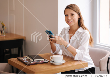 Businesswoman using phone during break in cafe. Female have rest and drink coffee 105528264