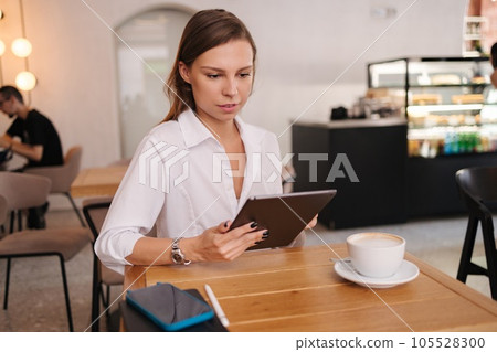 Female freelancer working in cafe using digital tablet. Young business manager drink coffee during work break Female freelancer working in cafe using digital tablet. Young business manager drink coffee during work break 105528300