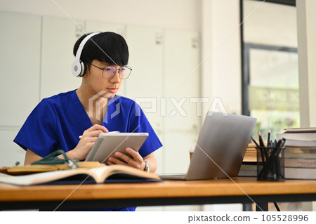 Concentrated medical student man wearing headphone and watching online lecture on laptop. Medical internship concept 105528996