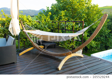 Hammock hangs on wooden terrace with table at a vineyard. Concept of paradise corner in industrial district of big city. Hammock hangs on wooden terrace with table at a vineyard. Concept of paradise corner in industrial district of big city. 105529244