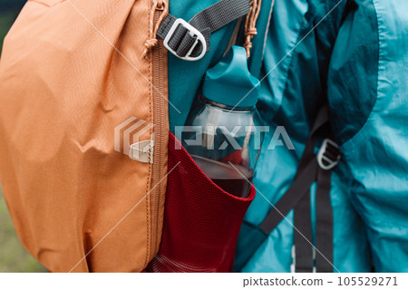 Close up of woman with water bottle in backpack pocket. Travel, tourism, hike and people concept. Rear view of male backpackers walking in field 105529271