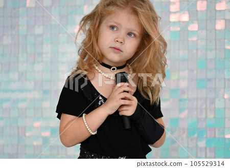 Portrait of a pretty little girl in a black dress singing karaoke 105529314
