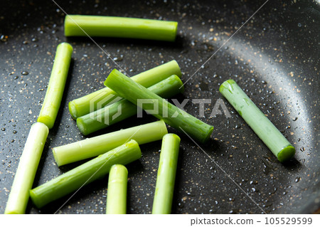 A cooking scene where garlic sprouts are fried in a frying pan. 105529599