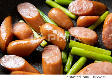 煎鍋裡煎香腸和蒜苗的烹飪場景。 煎鍋裡煎香腸和蒜苗的烹飪場景。 105529802