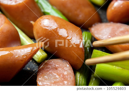 A cooking scene where wiener sausage and garlic sprouts are fried in a frying pan. 105529803