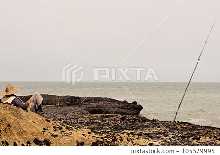 A Relaxed Fisherman Awaits His Catch Against a Beautiful Coastal Backdrop A Relaxed Fisherman Awaits His Catch Against a Beautiful Coastal Backdrop 105529995