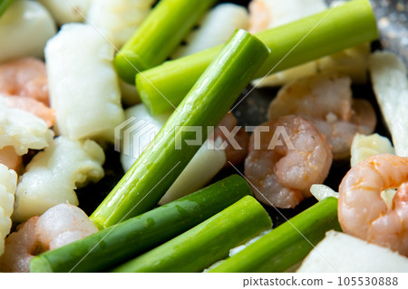 海鮮(魷魚和蝦)和蒜苗在煎鍋中煎炸的烹飪場景。 海鮮(魷魚和蝦)和蒜苗在煎鍋中煎炸的烹飪場景。 105530888