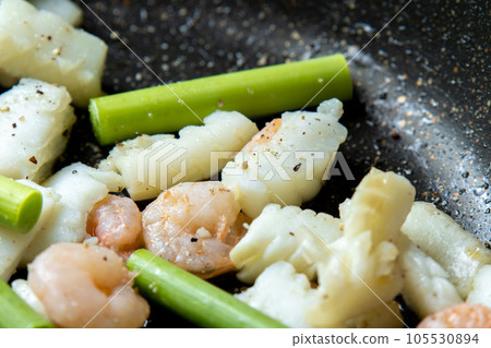 海鮮(魷魚和蝦)和蒜苗在煎鍋中煎炸的烹飪場景。 海鮮(魷魚和蝦)和蒜苗在煎鍋中煎炸的烹飪場景。 105530894