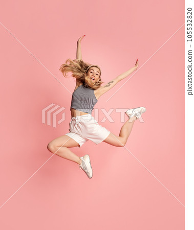 Portrait of cheerful positive girl jumping in the air with raised fists looking at camera isolated on light pink background. 105532820