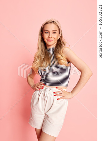 Portrait of smiling young woman dressed stylishly looking at camera against light pink studio background. Portrait of smiling young woman dressed stylishly looking at camera against light pink studio background. 105532821