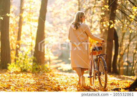 Stylish woman with a bicycle enjoying autumn weather in the park. Beautiful Woman in the autumn forest. 105532861