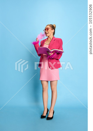Full lenght photo of excited girl wearing glamor in pink glasses, holding textbook looking away on light blue studio background. 105532906