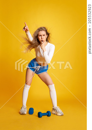 Full body shoot of young strong woman wear sporty with windblown hair looking at camera and whistle over yellow background. 105532923