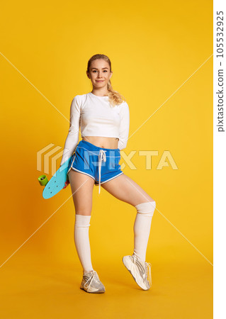 Full lenght shoot of smiling young girl wearing sportswear with ponyboard over yellow background. Exercises 105532925