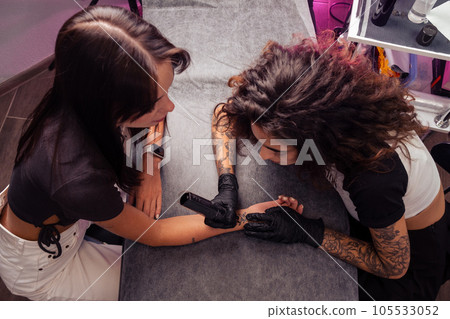 Professional female tattooist creating airplane tattoo on girl wrist 105533052