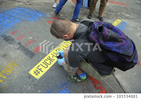 Young man activist painting offensive lettering against Putin on asphalt with a can spray. Kyiv, Ukraine Young man activist painting offensive lettering against Putin on asphalt with a can spray. Kyiv, Ukraine 105534881
