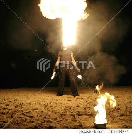 Man fire juggler performing at night on a sandy beach 105534885