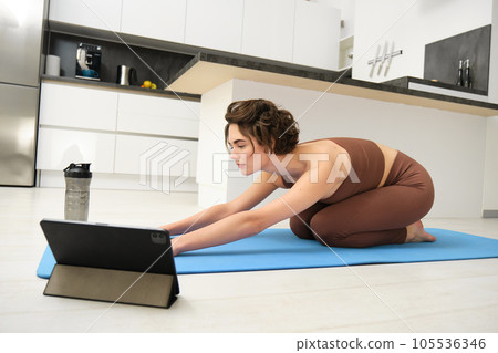 Image of young sportswoman does yoga at home, watches gym instructor tutorial video on tablet, stretches body, fitness training exercises, pilates class online from home 105536346