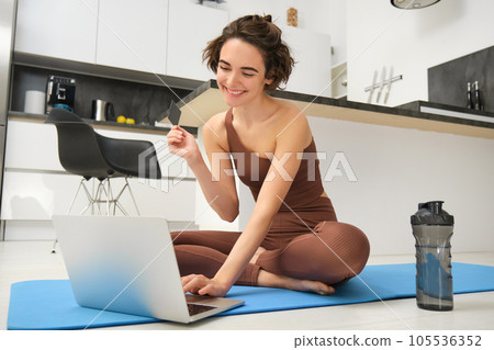 Image of young fitness girl, female athlete at home, workout on kitchen floor, holding credit card with laptop, purchasing online training session, gym application for home workout Image of young fitness girl, female athlete at home, workout on kitchen floor, holding credit card with laptop, purchasing online training session, gym application for home workout 105536352
