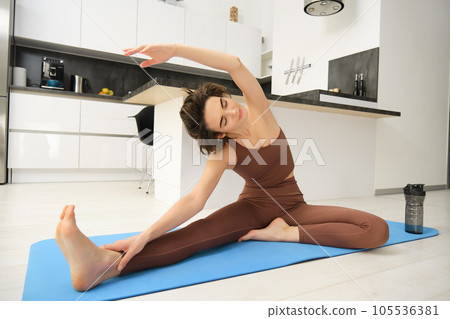 Image of brunette girl, stretching her legs, doing fitness workout, feet exercises to warm up before yoga, training at home alone Image of brunette girl, stretching her legs, doing fitness workout, feet exercises to warm up before yoga, training at home alone 105536381