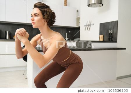 Workout and women wellbeing concept. Young fitness woman, doing squats, workout from home without gym equipment, training in bright room 105536393