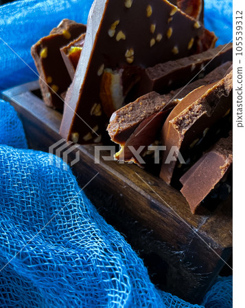 Pieces of chocolate with nuts and raisins on a dark background 105539312