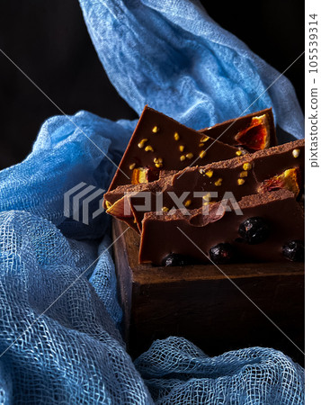 Pieces of chocolate with nuts and raisins on a dark background Pieces of chocolate with nuts and raisins on a dark background 105539314