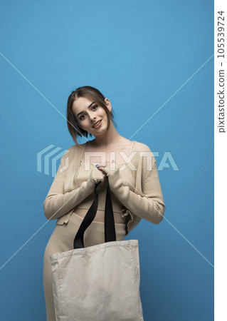 Brunette cheerful millennial woman holding white eco bag standing over white studio background. Lady holding flax shopper handbag. Fashion and ecology concept. 105539724