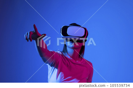Brunette woman in VR headset looking up at the objects in virtual reality. VR is a computer technology that simulates a physical presence and allows the user to interact with environment. Brunette woman in VR headset looking up at the objects in virtual reality. VR is a computer technology that simulates a physical presence and allows the user to interact with environment. 105539734