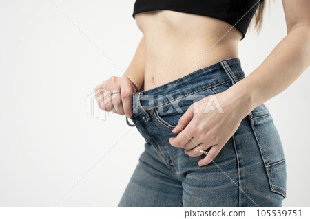 Slim woman showing slim body after sport trainings, healthy eating. Weight loss concept. Dieting. Thin woman in big blue jeans pants, weight loss concepts. Slim girl wearing oversized pants. 105539751
