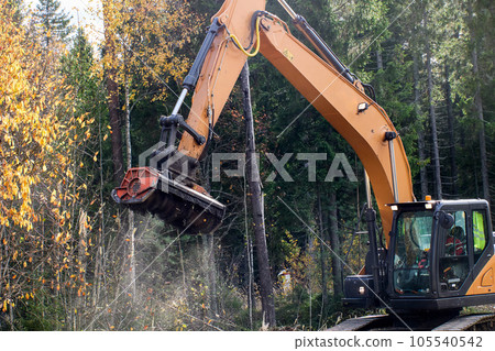 Wood chipper is chopping wood on side of road using mulching attachment on an excavator. 105540542