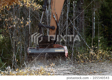 Forestry mulcher shreds wood on side of road using mulching attachment on excavator. 105540543