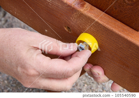Using steel fasteners when assembling outdoor furniture, assembler joins two boards together. 105540590