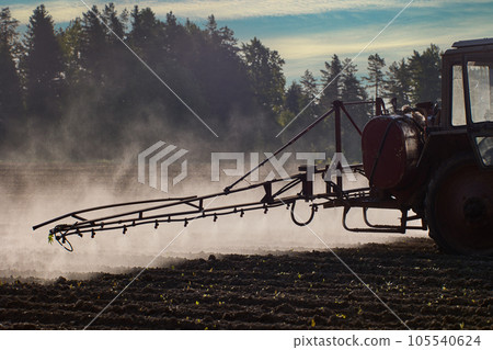 An aerosol cloud behind farm tractor spraying herbicides in potato field. 105540624