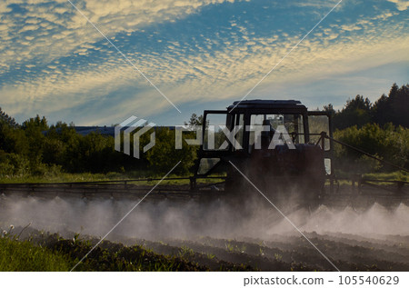 Spraying herbicides on an agricultural field with sprayer on boom mounted to tractor. 105540629