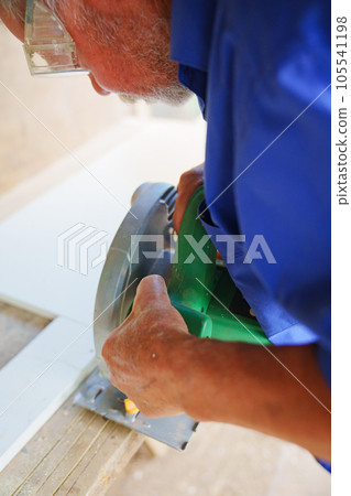 an elderly man in goggles with a circular saw an elderly man in goggles with a circular saw 105541198