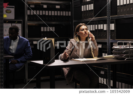 Manager having remote talk with businessman, working overtime at accountancy report arhive room. Confident repository employee organizing administrative files, searching for management research Manager having remote talk with businessman, working overtime at accountancy report arhive room. Confident repository employee organizing administrative files, searching for management research 105542009
