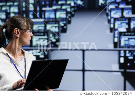 Experienced technician in data center working on laptop, setting up high bandwidth dedicated multiplayer online gaming servers to accommodate more traffic from worldwide locations Experienced technician in data center working on laptop, setting up high bandwidth dedicated multiplayer online gaming servers to accommodate more traffic from worldwide locations 105542054