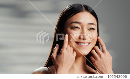 Positive model with luminous skin creating beauty ad, with cosmetics for glowing radiant appearance. Asian woman posing in studio and advertising body positivity campaign on camera. 105542096