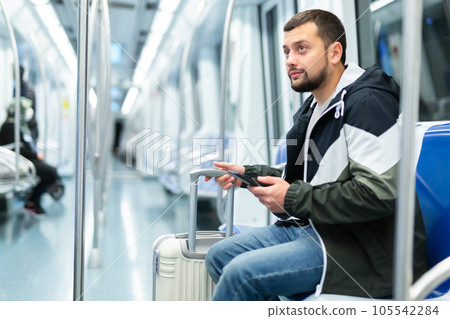 Bearded traveler sitting with suitcase and smartphone in metro car Bearded traveler sitting with suitcase and smartphone in metro car 105542284