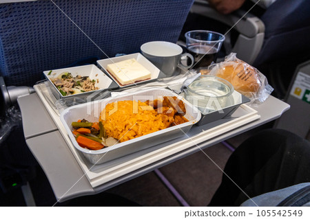 Inflight airplane Asian food set meal served consisting rice and spicy chicken, appetizer, dessert, bun and red wine Inflight airplane Asian food set meal served consisting rice and spicy chicken, appetizer, dessert, bun and red wine 105542549